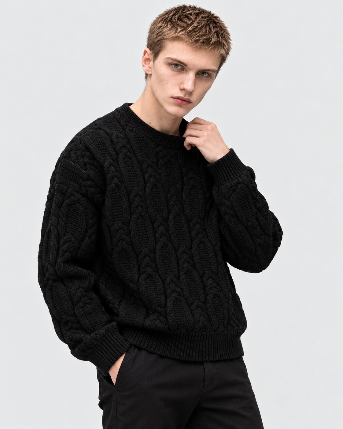 Image of Black | Male model wearing black cable-knit sweater with one hand at collar, angled pose