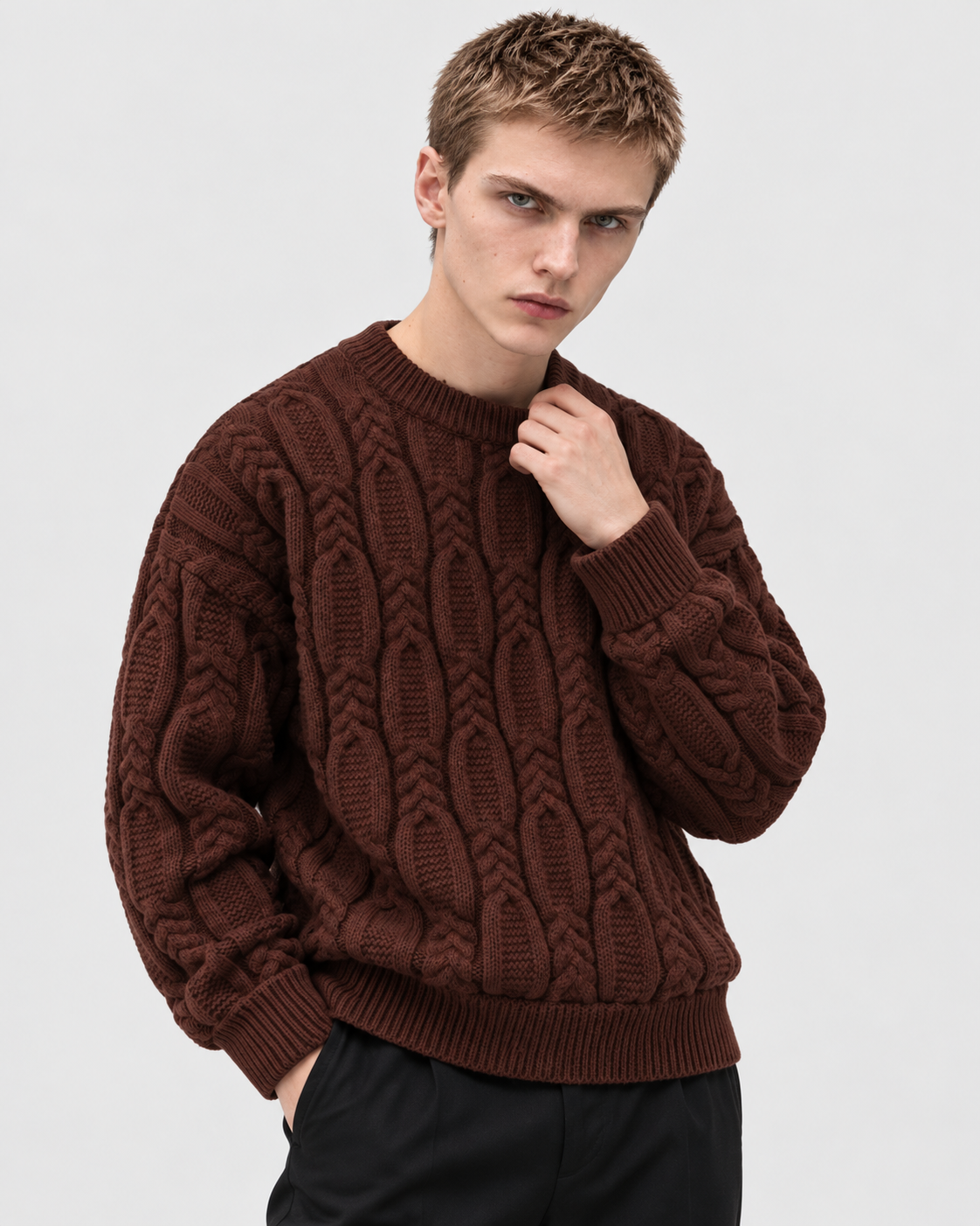Image of Coffee | Male model wearing coffee-brown cable-knit sweater, one hand near neck in studio pose