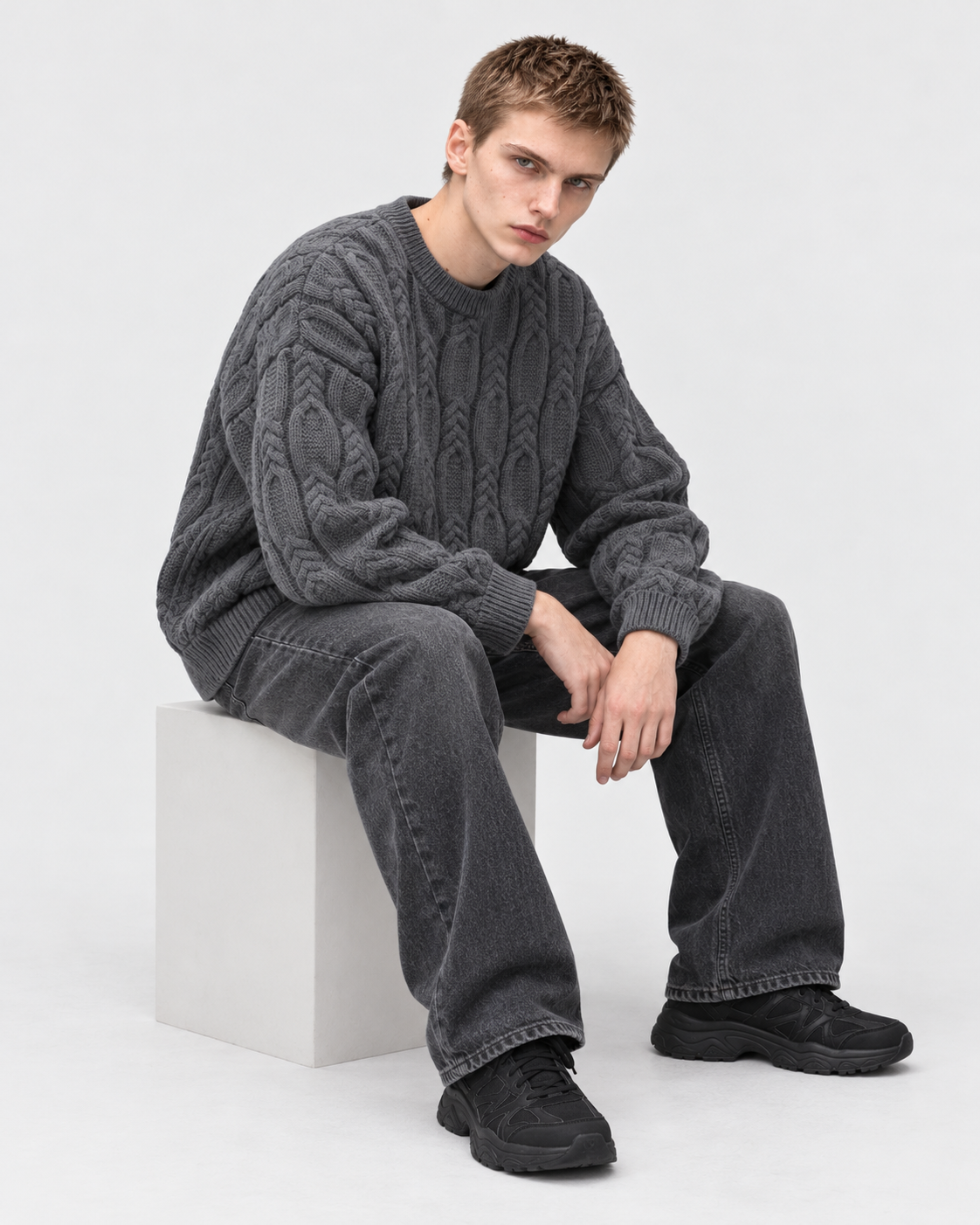 Image of Gray | Male model wearing gray cable-knit crewneck sweater, seated studio pose