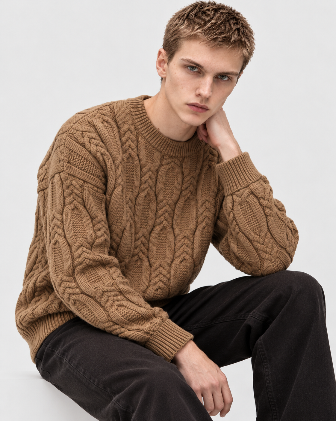 Image of Khaki | Male model wearing khaki cable-knit sweater, seated side studio pose