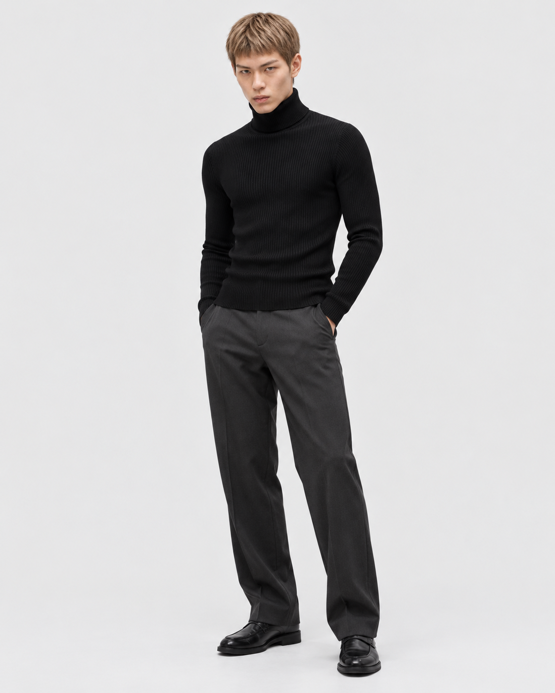 Black | Male model wearing a fitted black ribbed turtleneck sweater with dark trousers in a standing pose