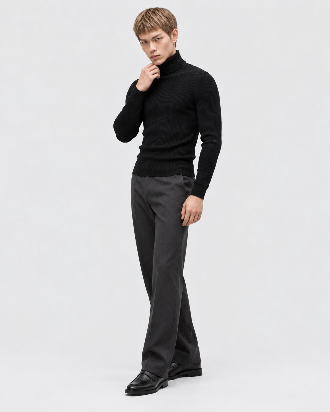 Image of Black | Male model wearing a black ribbed turtleneck sweater with one hand raised near his face