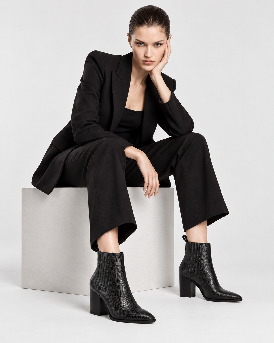 Image of Black | Seated model wearing black snakeskin-print pointed-toe ankle boots